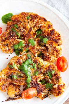 a white plate topped with two pieces of fried cauliflower next to tomatoes and broccoli