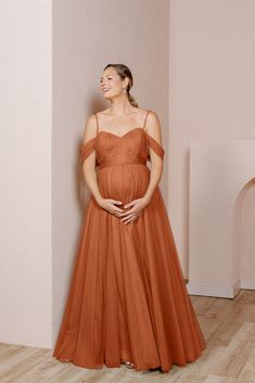 a pregnant woman in an orange dress standing against a wall