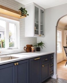 a kitchen with blue cabinets and white counter tops next to a dining room table in front of a window