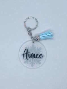 an acrylic keychain with the word aime on it and a blue tassel