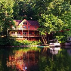 a house sitting on the shore of a lake surrounded by green trees and lush greenery