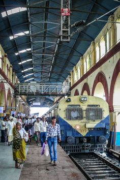 people are walking along the train tracks in an indoor station with a yellow and blue train parked next to it