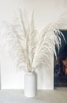 a white vase filled with lots of white feathers on top of a table next to a fireplace