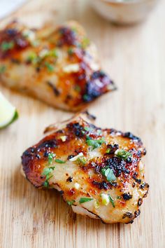 a piece of chicken on a cutting board next to some lemons and cilantro