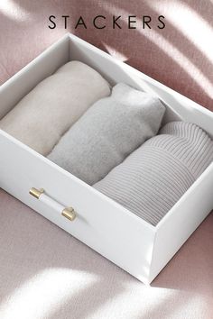 a white box with pillows and sweaters in it on a pink blanketed surface