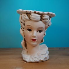 a white ceramic vase with a woman's head on it, sitting on a wooden table