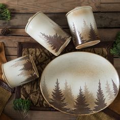 four cups and two plates on a table with pine trees painted on the side, surrounded by napkins