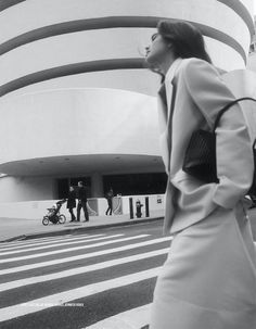 a woman walking across a cross walk in front of a building