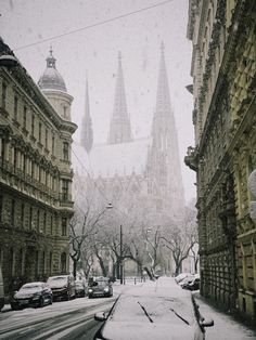 a snowy street with cars parked on the side and tall buildings in the back ground