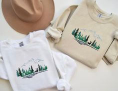 Forest National Park Embroidered Sweatshirt, Embroidered Forest National Park Shirt, Mountain Embroidered Sweatshirt, Deer Embroidered ShirT Wrap yourself in the tranquility of the wilderness with our 'Forest with Deer National Park' embroidered sweatshirt! This unique design brings the majesty of the great outdoors to life, featuring intricate embroidery of lush forests and graceful deer. Whether you're a nature enthusiast or simply seeking a touch of rustic charm, our sweatshirt is a perfect a White Long Sleeve Shirt With Machine Embroidery, White Long Sleeve Shirt With Embroidered Graphics, Fall Embroidered Crew Neck Shirt, Embroidered Crew Neck Shirt For Fall, White Embroidered Winter Tops, Winter White Embroidered Tops, Casual Long Sleeve Top With Contrast Embroidery, Casual Crew Neck Top With Contrast Embroidery, Casual Tops With Contrast Embroidery And Crew Neck