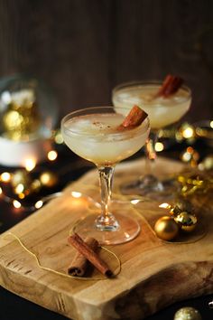 two glasses filled with white wine and cinnamon on top of a wooden tray next to christmas decorations