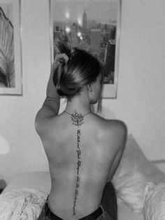 a woman with a tattoo on her back is sitting in bed and looking at the city