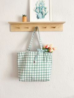 a green and white checkered tote bag hanging on a wall next to flowers