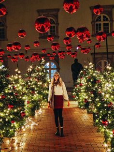 a woman standing in front of christmas trees with red balls hanging from it's ceiling