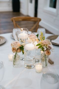 the table is set with candles, flowers and glass vases for centerpieces