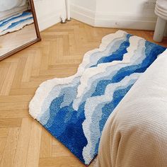 a blue rug on the floor next to a white bed and mirror in a room