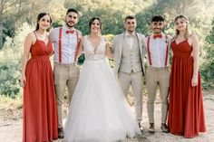 a group of people standing next to each other wearing red dresses and bow ties in front of trees