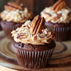 three cupcakes with frosting and pecans on top sitting on a plate