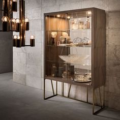 a wooden cabinet with glass doors and lights on it's sides, in front of a stone wall