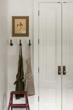 a coat rack with two coats hanging on it next to a white door and red stool