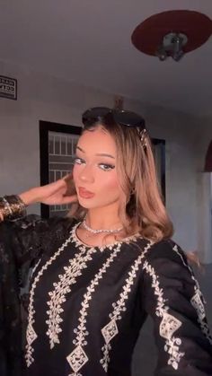 a woman in a black and white dress is holding her hand to her face while looking at the camera