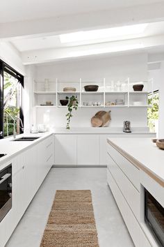 a white kitchen with lots of counter space and open shelves on the wall, along with an area rug