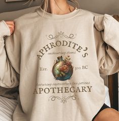 Welcome to Aphrodite's Apothecary, the best place to purchase love potions! This sweatshirt is inspired by the Greek pantheon of gods. A great halloween shirt or gift for those who simply love Greek mythology. *This sweatshirt is printed in the United States* *Made from 50% Cotton and 50% Polyester* Our sweatshirts are unisex. Please refer to the size chart in the picture for sizing.  For sweatshirt care, we recommend that you machine wash: warm; non-chlorine bleach as needed; Tumble dry: medium Greek Mythology Shirt, Aphrodite Inspired Outfits, Greek Goddess, Jewelry Outfit, Aphrodite, Sweatshirt Designs, Greek Mythology, Really Cute Outfits, Cute Tops