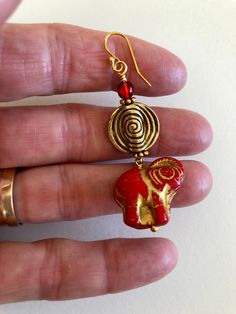 a hand holding onto a pair of gold and red earrings with an elephant head on it