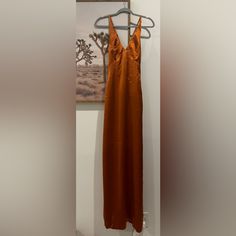 an orange dress hanging on a hanger in front of a wall with a painting