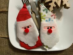 two santa claus napkins are on a plate with forks and spoons next to each other