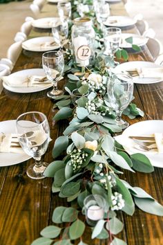 the table is set with white plates and silverware, greenery, and candles