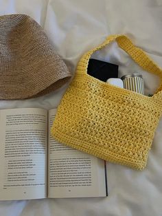 an open book and a crocheted bag on a bed with a straw hat