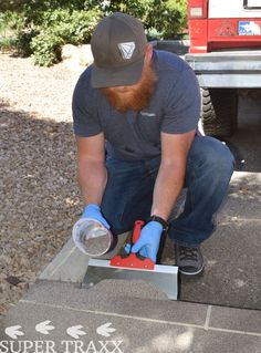 a man with a beard and blue gloves is working on a piece of metal in front of a truck