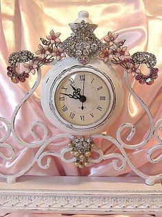 an ornate white clock with pink flowers on the front and sides, sitting on a stand