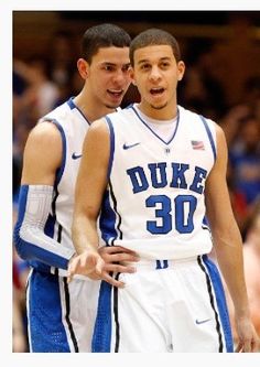 two young men standing next to each other in front of a crowd at a basketball game