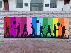 a group of children playing with a ball in front of a rainbow colored wall mural