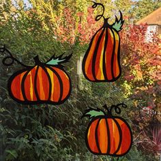 three pumpkins are hanging from a window in front of some bushes and trees with red leaves