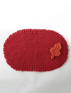 a red crocheted placemat with an orange flower on the center and a brown button in the middle