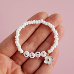 a hand holding a white beaded bracelet with the word lucky written in small letters