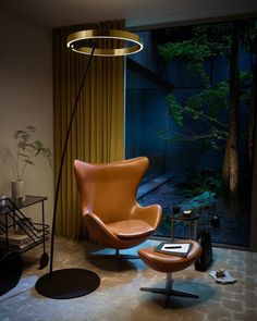 a modern living room with an orange leather chair and black round footstool in front of a large window