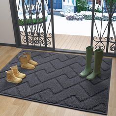 two pairs of rubber boots sitting on top of a gray rug in front of a glass door