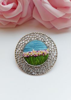 a brooch that is sitting on a table next to some flowers and pink roses