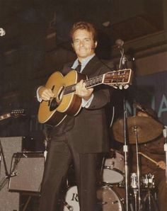 a man in a suit and tie playing an acoustic guitar while standing next to a microphone