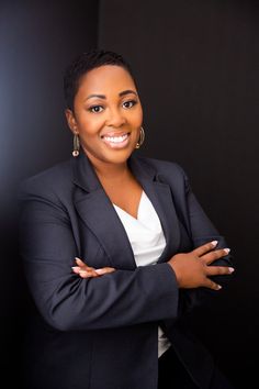 a woman with her arms crossed in front of a black background wearing a blazer and white shirt