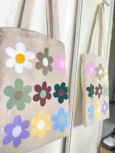 two bags with flowers painted on them hanging from the wall next to a pair of shoes