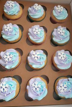 twelve cupcakes with frosting and snowflakes on them in a box