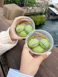 two plastic cups filled with green donuts on top of a wooden table next to a body of water