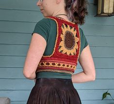 a woman wearing a crocheted sunflower top and brown leather skirt standing in front of a blue house