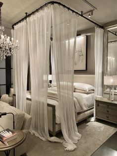 a white canopy bed sitting in a bedroom next to a chandelier