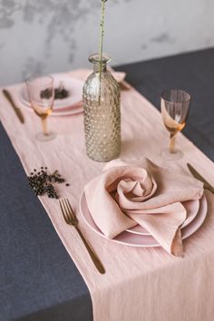 the table is set with plates, silverware and a pink rose in a vase